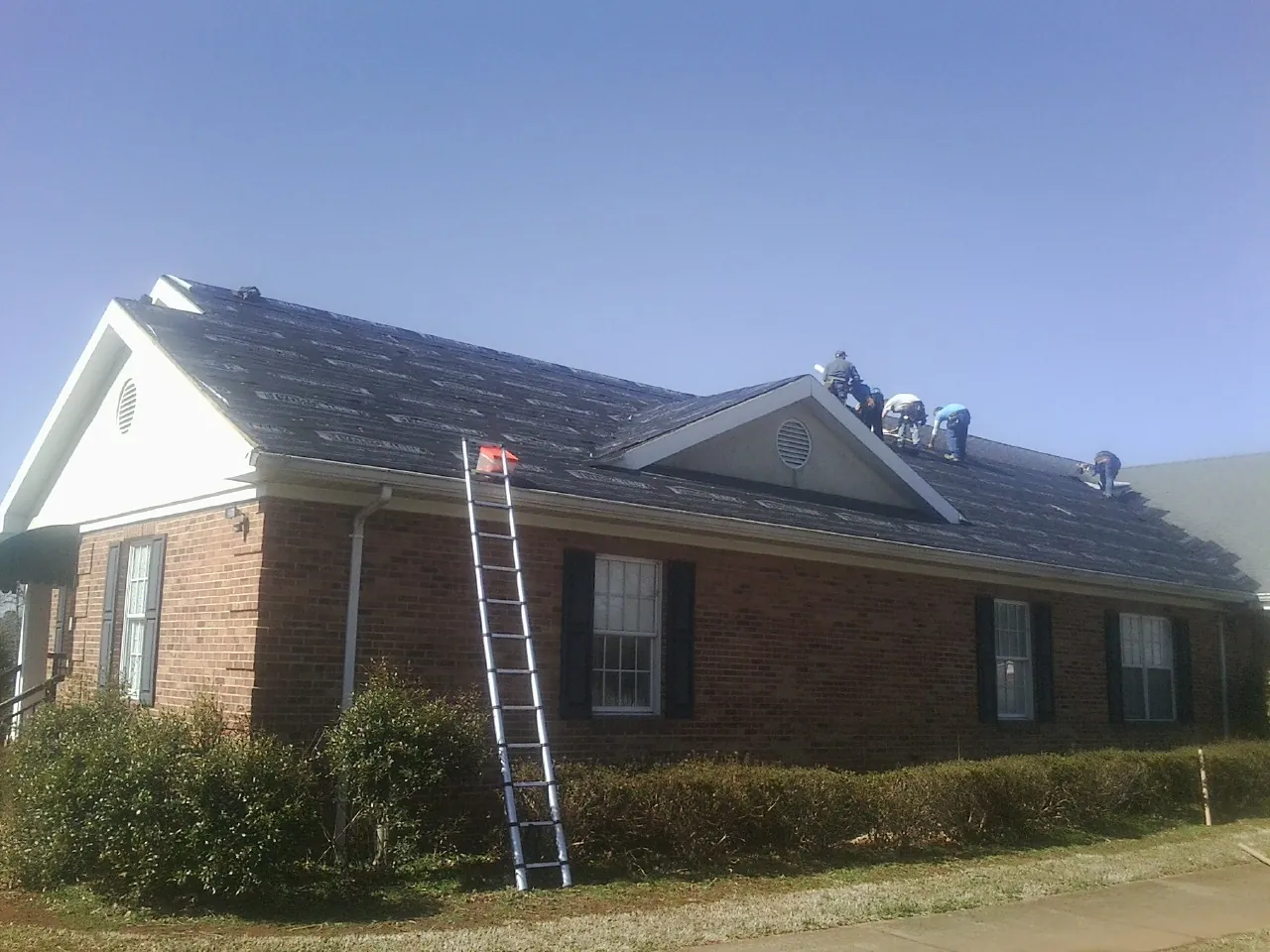 Crew tearing shingles off a brick ranch roof with a ladder set — Metal Roof Repair work by our crew in Nehalem