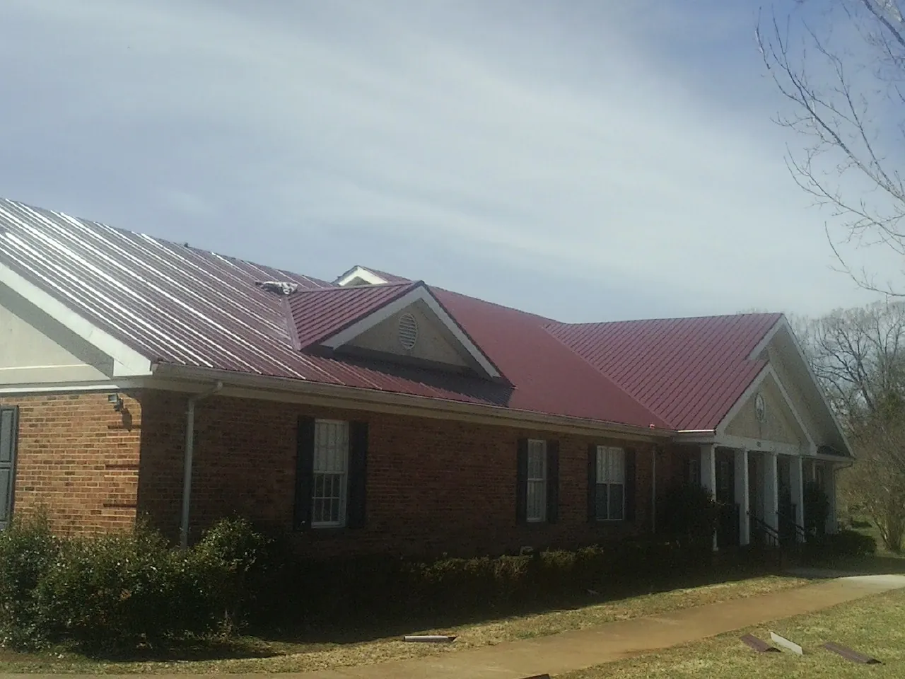 Red metal roof with gabled entries on a long brick building, from a Hail Damage Roof Repair job in Nehalem