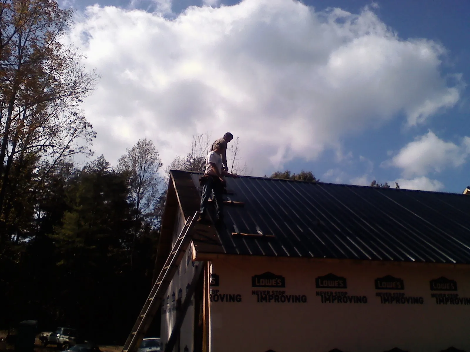 Roofer fastening dark metal panels high against a cloudy sky, from a Roof Inspection job in Nehalem