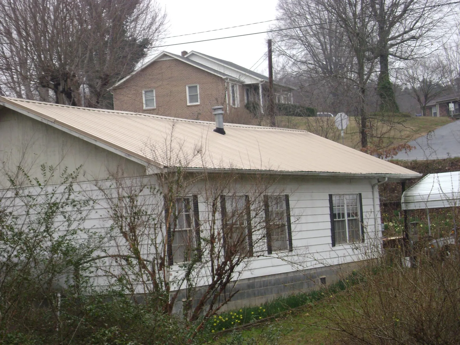 Tan metal roof on a white sided house set into a hillside — Commercial Roofing by Roofing Brothers in Nehalem